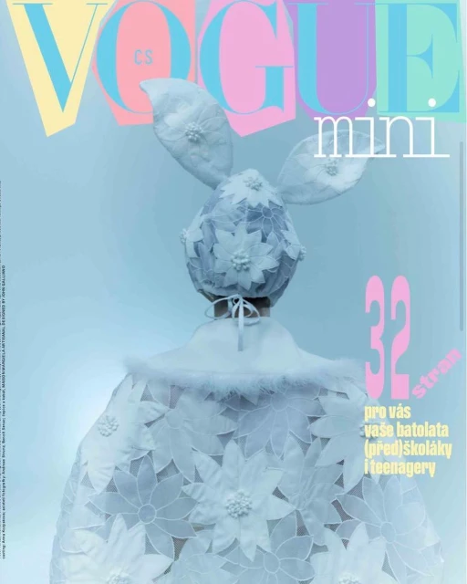 Vogue Mini magazine cover features child model wearing a white floral lace bunny-eared hat and cape against light blue backdrop.