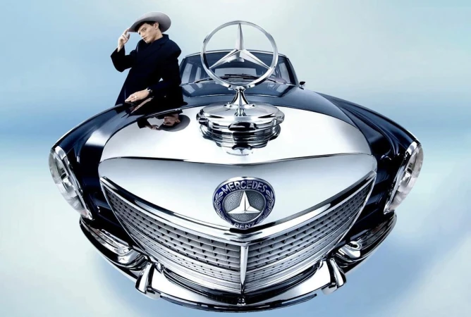 A stylish man in a hat and coat leans on a vintage Mercedes-Benz. Close-up emphasizes the car's chrome details and classic design.
