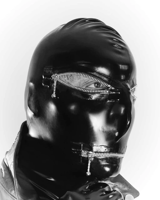 Person wearing black latex mask with zippers over mouth and eyes in a studio shot, creating an edgy and unique fashion statement.