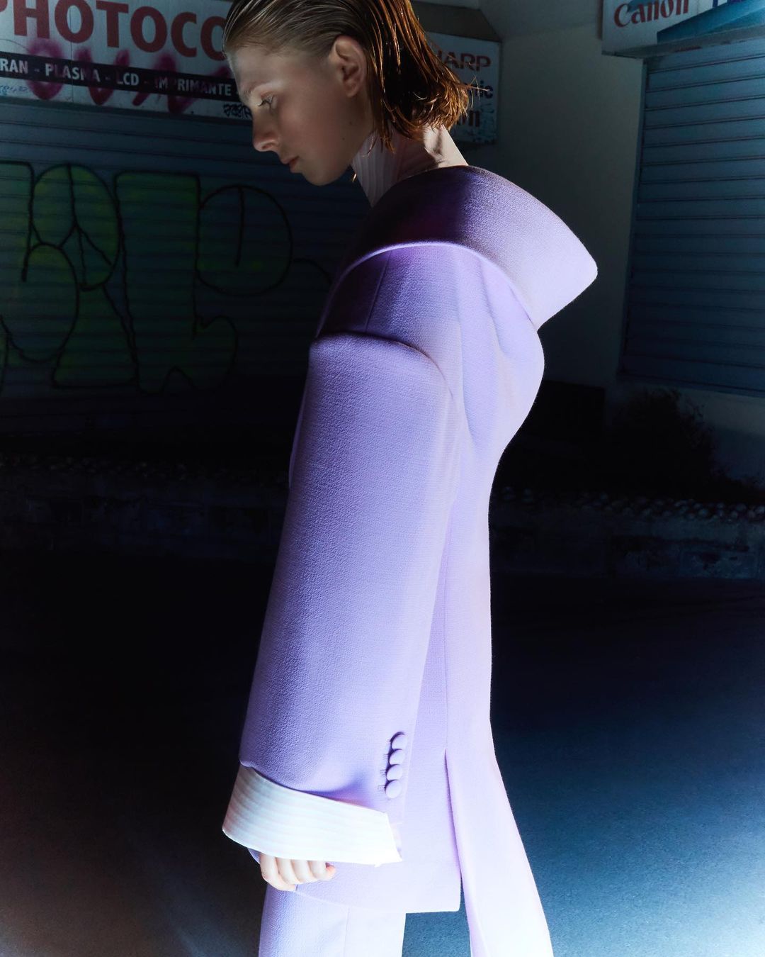 Woman in a lavender suit posing in front of a graffiti wall. The shot is taken with a medium frame and focuses on the woman's profile.