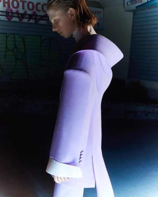 Woman in a lavender suit posing in front of a graffiti wall. The shot is taken with a medium frame and focuses on the woman's profile.