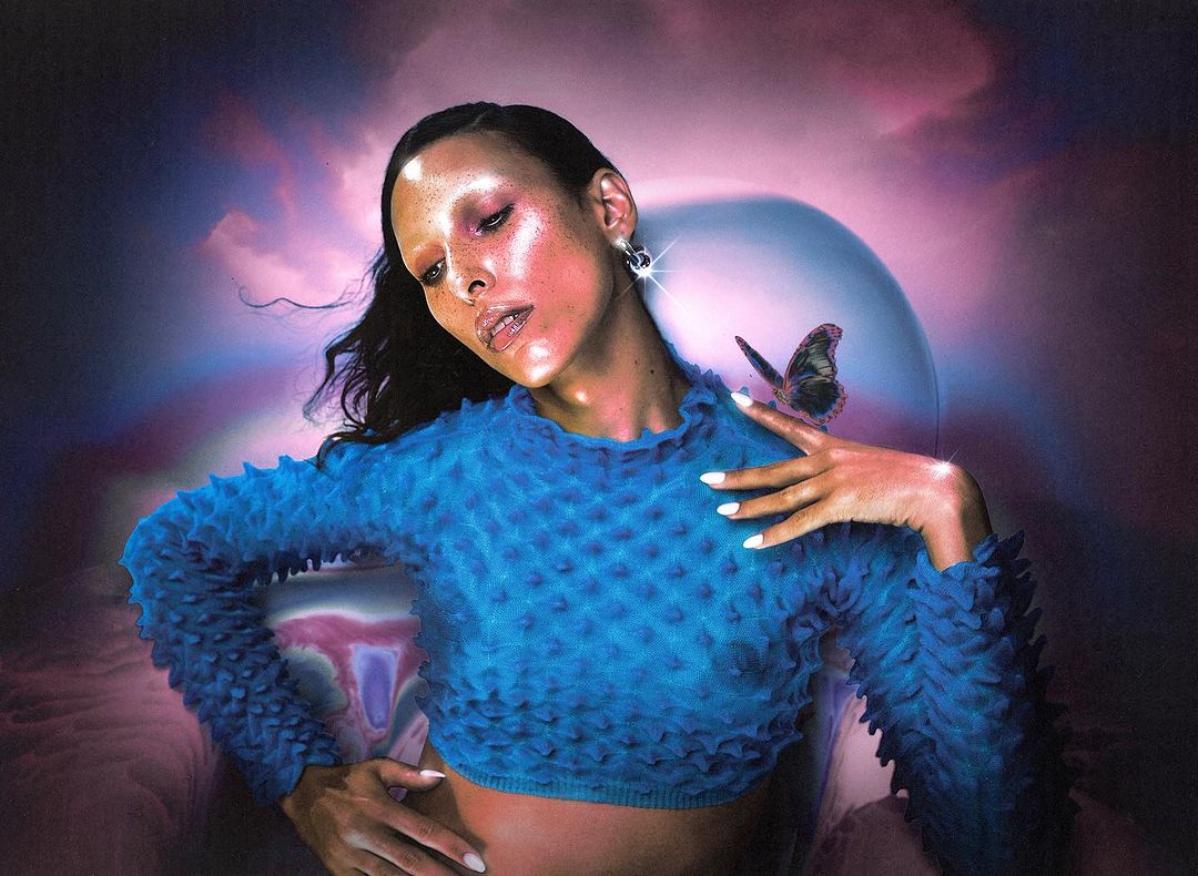 Elegant woman with a butterfly on her shoulder posing indoors against a dreamlike background with surreal colors and diffused lighting.
