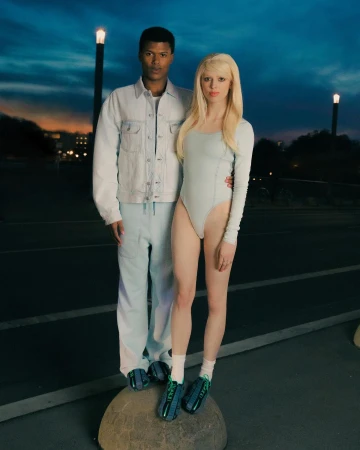 Man in denim jacket and woman in light blue bodysuit standing on a stone sphere outdoors at dusk by Tereza Mundilova