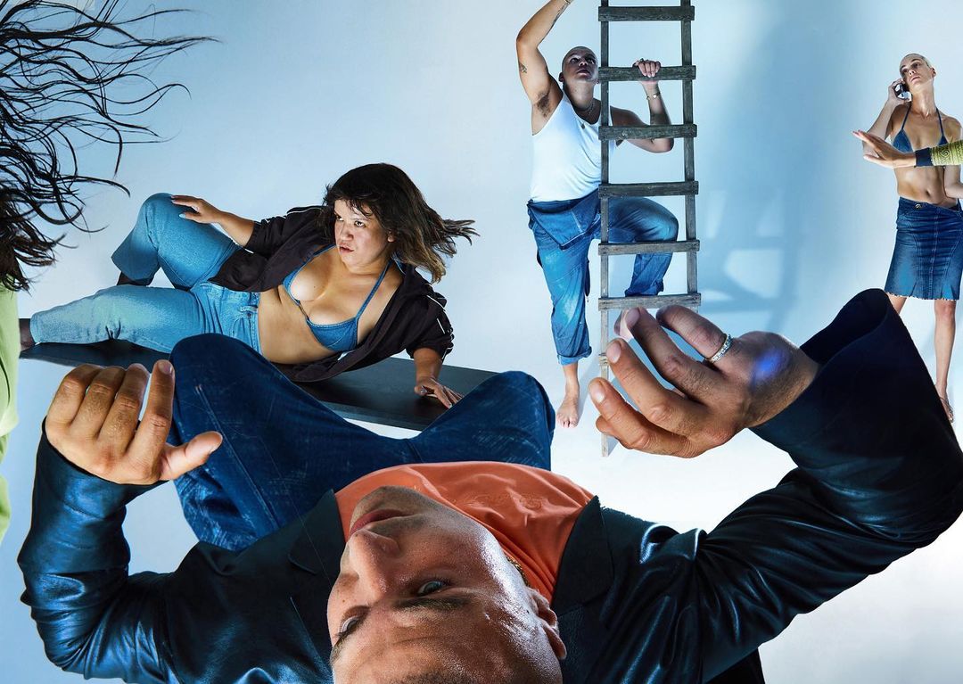 Group of five people in a studio setting, including a man climbing a ladder and others in various poses, against a light blue background.