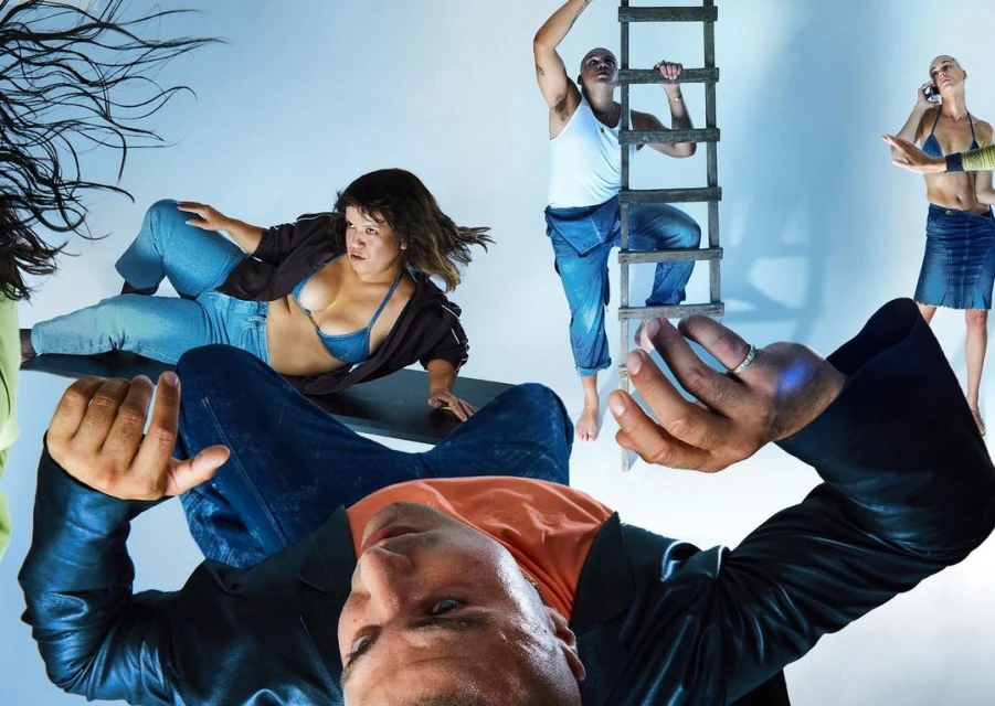 Group of five people in a studio setting, including a man climbing a ladder and others in various poses, against a light blue background.