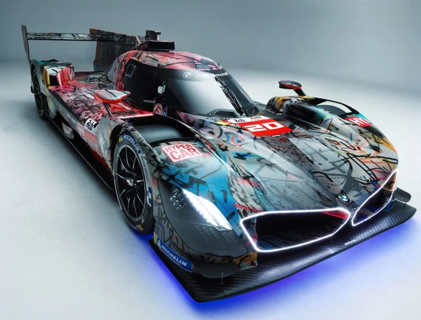 Eye-level, wide shot of a BMW M Hybrid V8 race car with an artistic design, captured in a bright photo studio with a soft, white background.