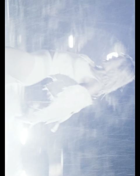 Abstract, blurry image of a female figure in a bright, airy space. The photograph is shot with a strong light source creating a dreamy aesthetic.