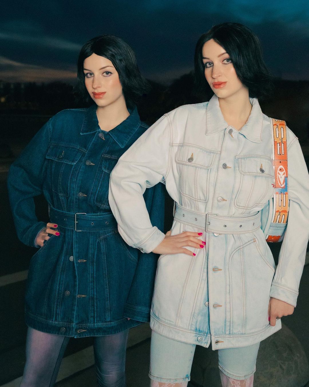 Two women in denim jackets and knee-high socks pose outdoors against a twilight sky. One jacket is dark denim; one is light denim.