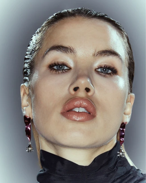 Close-up portrait of a woman with slicked-back hair and glossy lips, wearing statement earrings against a gradient grey background.
