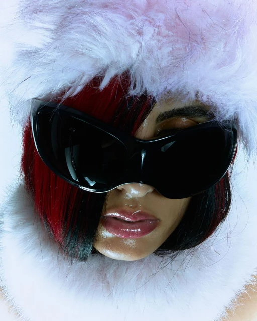 Close-up shot of a person wearing black sunglasses and a feathered hat with red and black hair, focusing on fashion and accessories.
