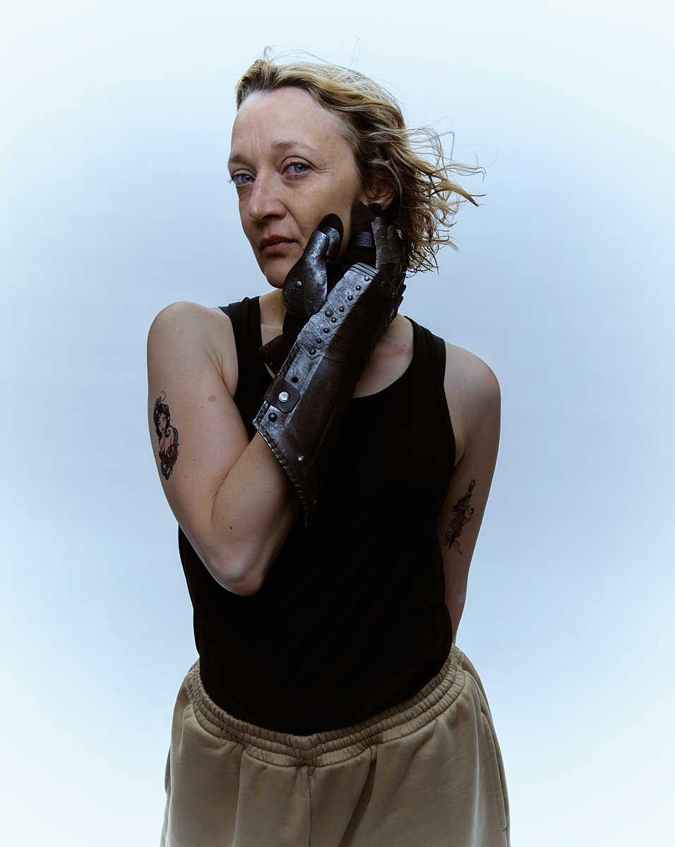 Woman with prosthetic hand poses indoors. Close-up portrait with blonde hair and a black tank top, standing against a bright backdrop.