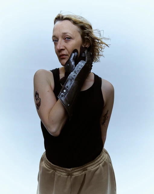 Woman with prosthetic hand poses indoors. Close-up portrait with blonde hair and a black tank top, standing against a bright backdrop.