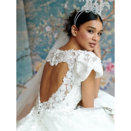 Elegant bride poses in white lace gown and tiara against a blue floral backdrop, showcasing a refined and classic bridal look.