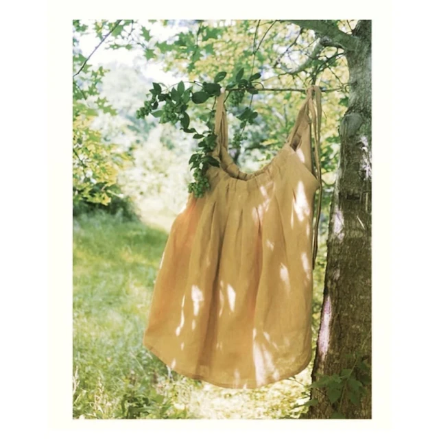 Tan fabric tote bag with vine draped over the handle hangs on a tree branch in a bright outdoor setting with blurred foliage background.