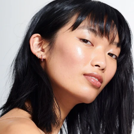 Close-up portrait of an East Asian woman with glossy dark hair and radiant skin wearing small hoop earrings.