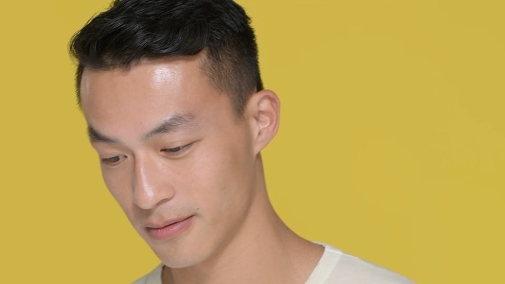 Close-up portrait of an East Asian man looking down against a solid yellow background by photographer Terry Doyle.