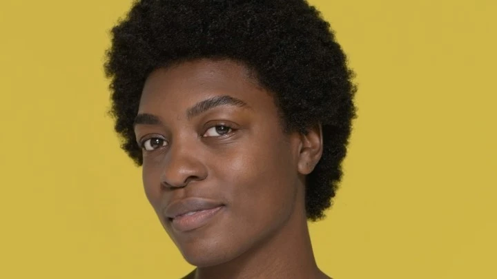 Portrait of an African American woman with an afro against a bright yellow background, showcasing natural beauty and a serene expression.