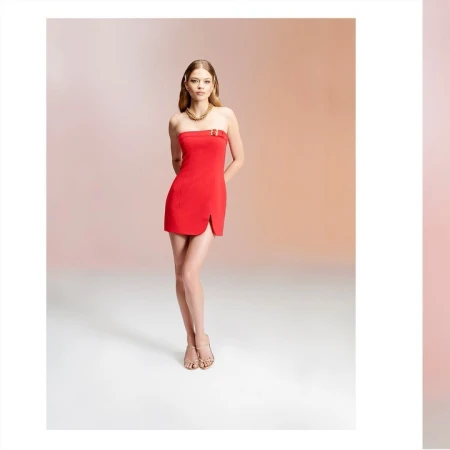 Model in a strapless red minidress and gold necklace standing against a gradient studio backdrop.