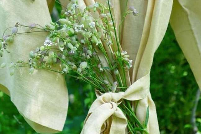 Close-up of a bouquet of wildflowers tied with light beige fabric against a blurred natural green background.