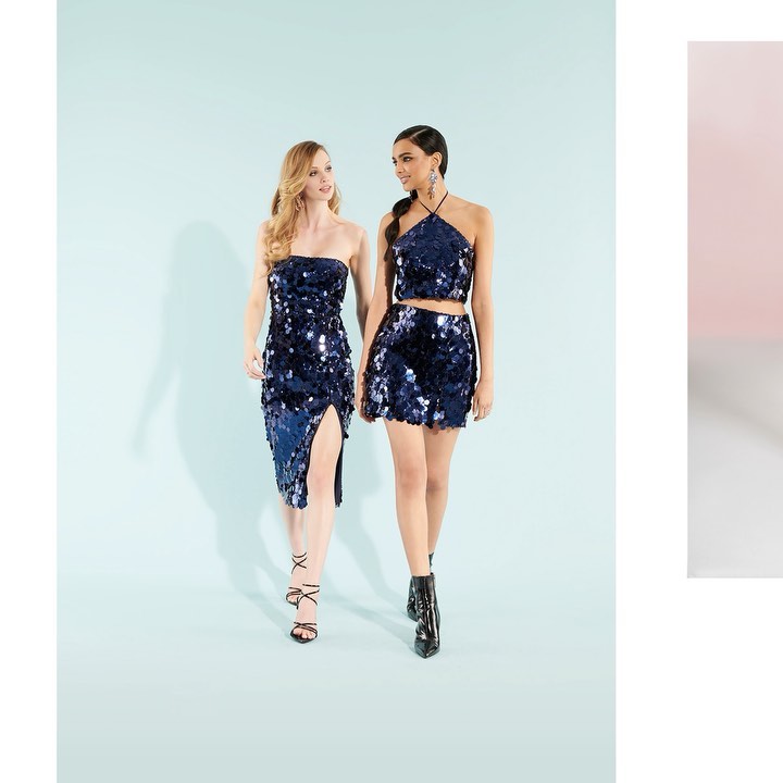 Two adult females in sequined dresses pose in a fashion forward, full shot against a light blue backdrop, showcasing modern style.
