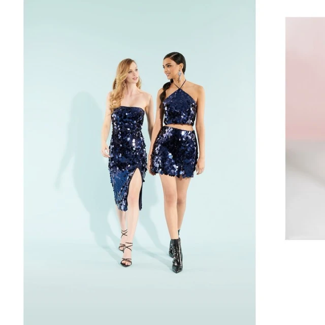 Two adult females in sequined dresses pose in a fashion forward, full shot against a light blue backdrop, showcasing modern style.