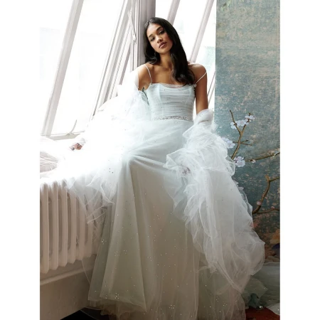 Woman in an elegant, light blue gown sitting near a window with natural light, creating a soft, dreamy atmosphere. Fashion shot.