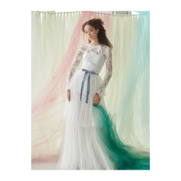 Woman wearing a white lace long sleeve wedding dress with a blue bow belt against pastel fabric drapes
