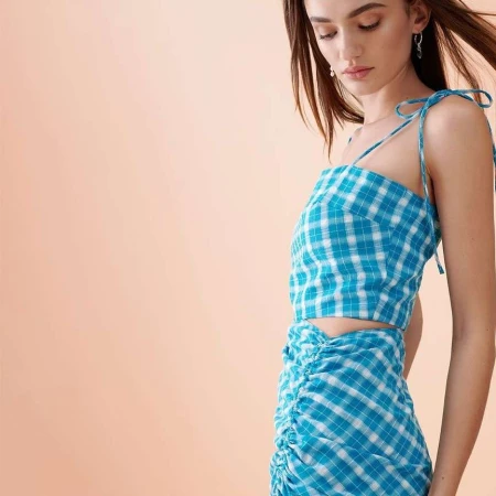 A woman wearing a blue and white plaid two-piece outfit against a solid peach-colored background.