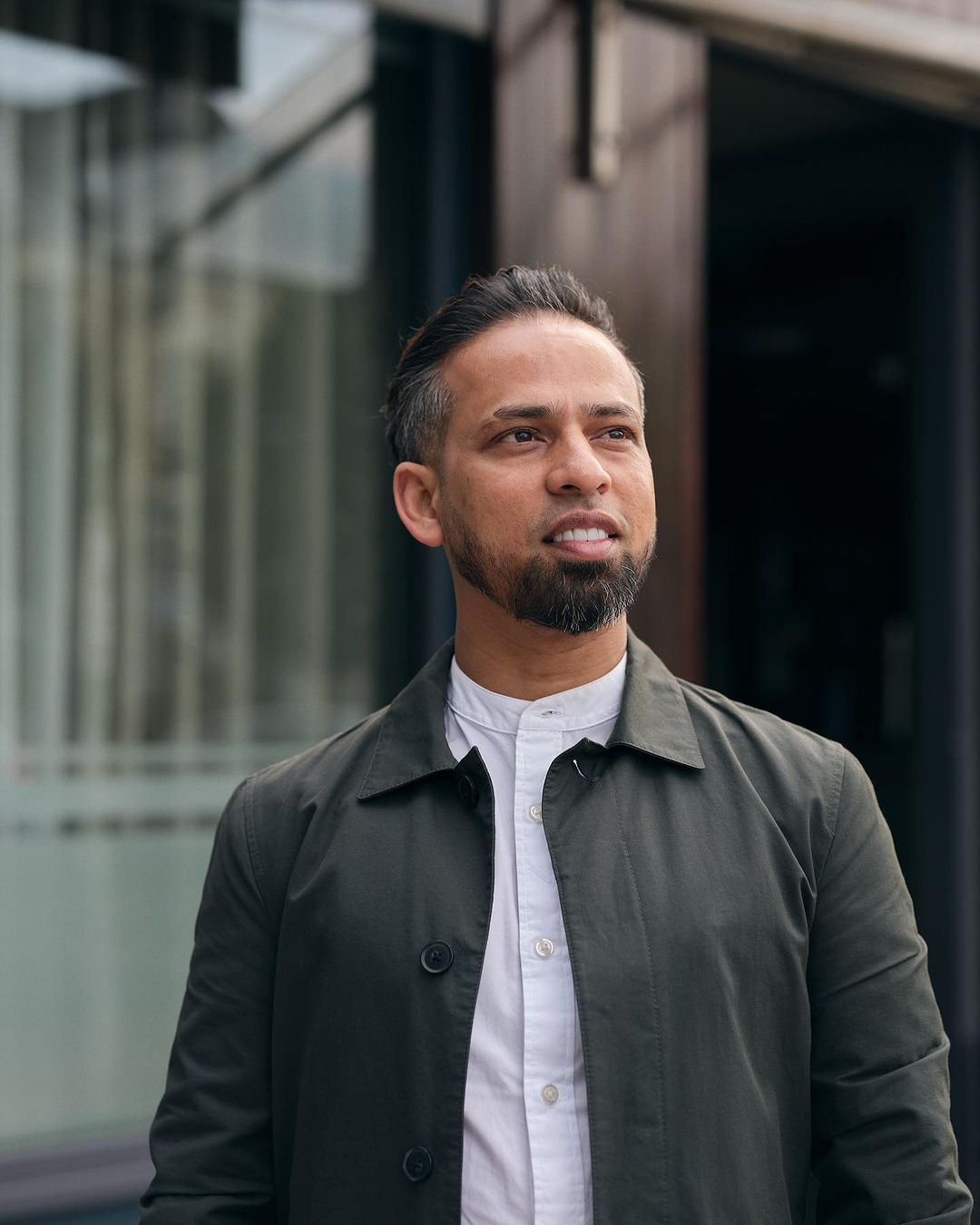 Portrait of adult male wearing a collared shirt and a jacket, outside in an urban setting with blurred background in daylight.