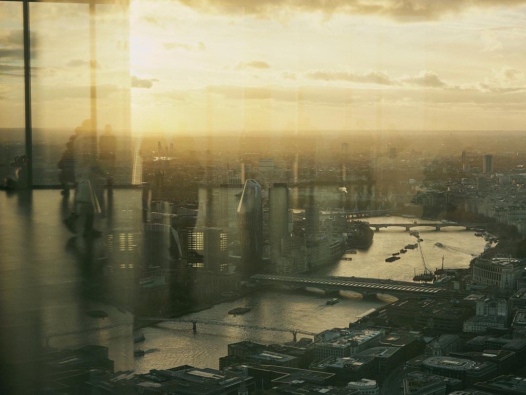 High-angle view of the London skyline with modern architecture, bridges over the river, and a golden sunset, creating a serene urban landscape.