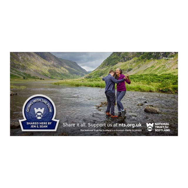 Couple dances on rocks in stream against scenic backdrop of mountains and cloudy sky; advertisement for the National Trust for Scotland.