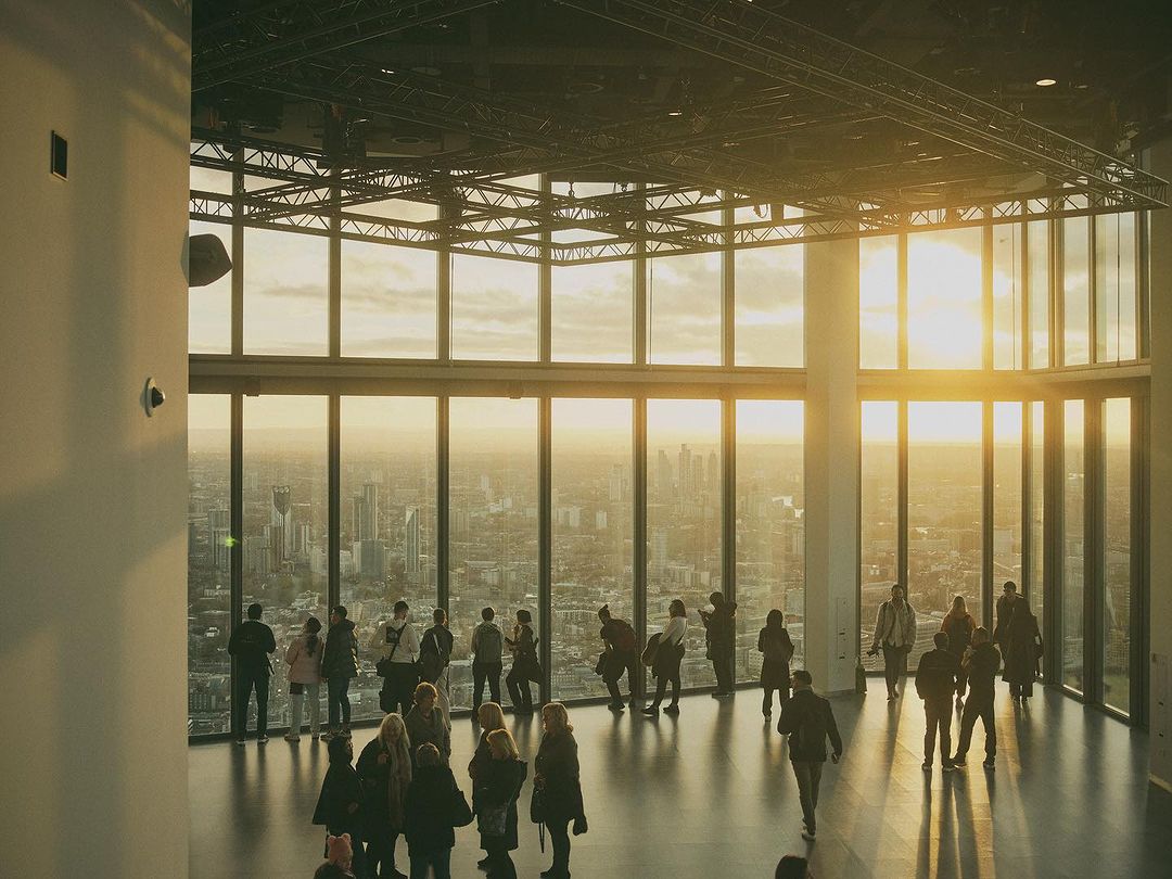 Elevated view of a group of people gathered in a modern building with floor-to-ceiling windows overlooking a cityscape during daytime.