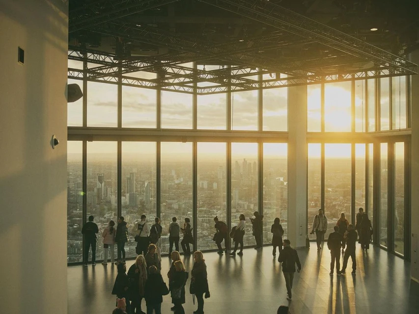 Elevated view of a group of people gathered in a modern building with floor-to-ceiling windows overlooking a cityscape during daytime.