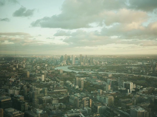 High-angle aerial view of London's skyline featuring numerous buildings, a winding river, and a cloudy sky during daylight.
