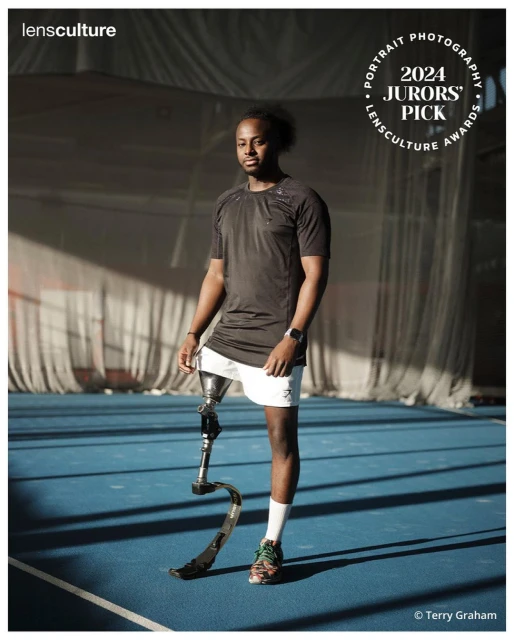 A full shot of a man with a prosthetic leg stands on an indoor court in athletic wear with soft natural lighting and a shallow depth of field.