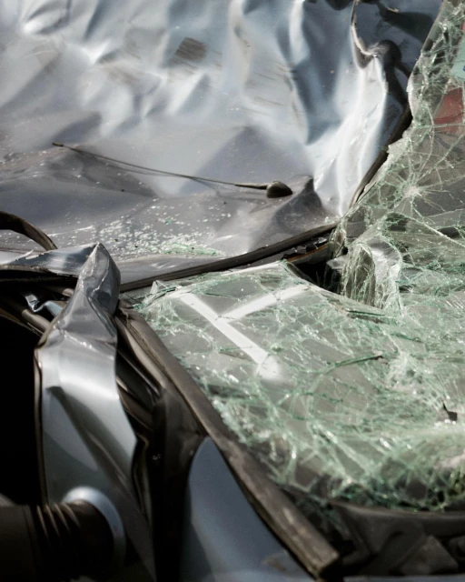 Damaged silver car with shattered windshield after accident, showing crumpled metal and broken glass, highlighting the severity of the impact.