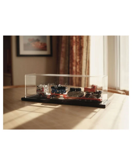 Display case featuring miniature truck models, set on a wooden surface against a backdrop of curtains and a framed picture.