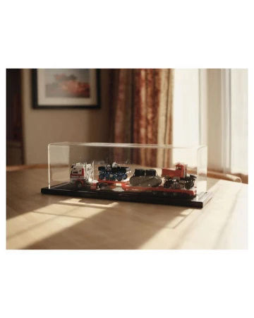 Display case featuring miniature truck models, set on a wooden surface against a backdrop of curtains and a framed picture.