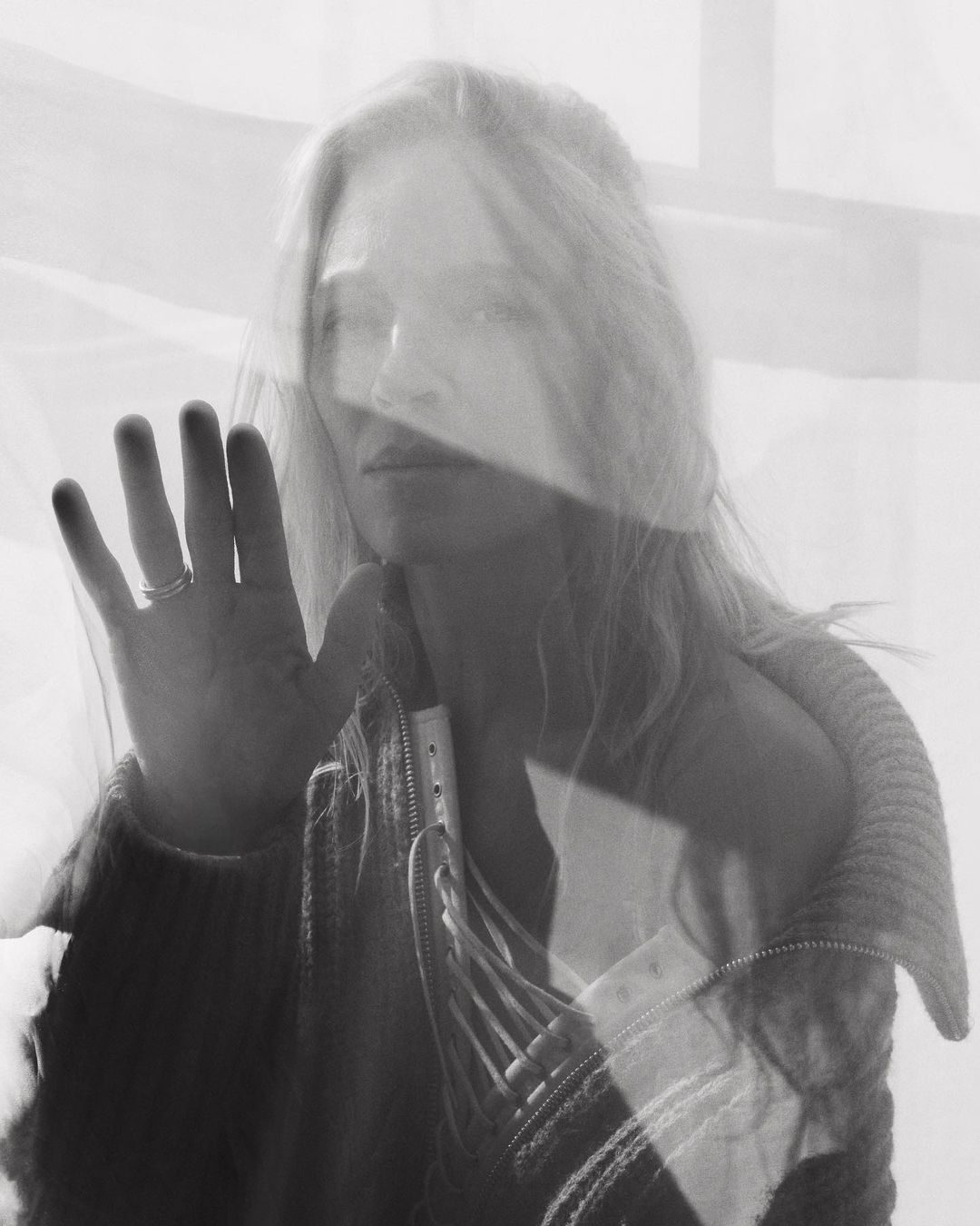 Monochrome portrait of a woman pressing her hand against a translucent layered surface by Tess Ayano.