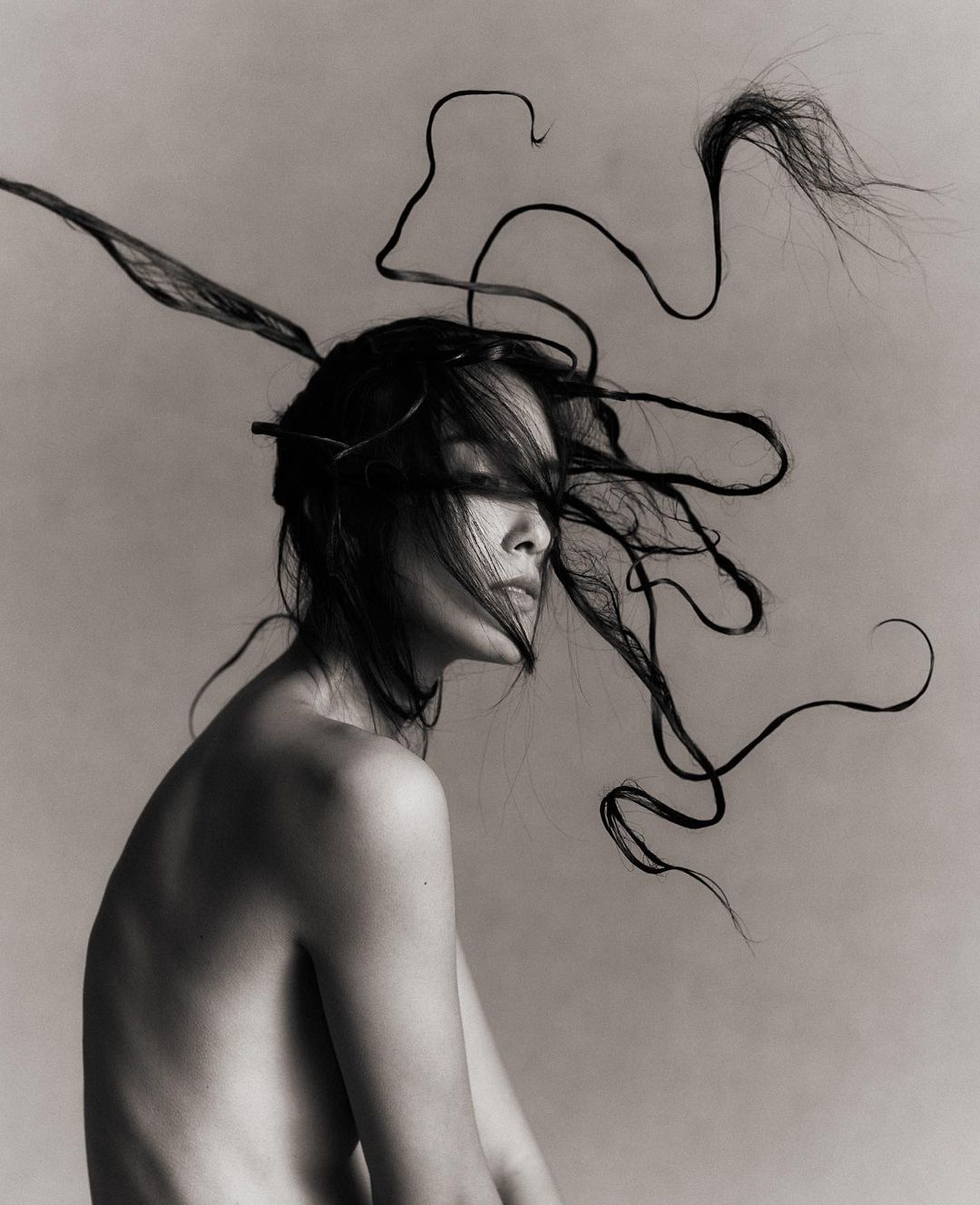 Artistic black-and-white portrait of a bare-shouldered woman with stylized hair, emphasizing creative beauty and photographic technique.