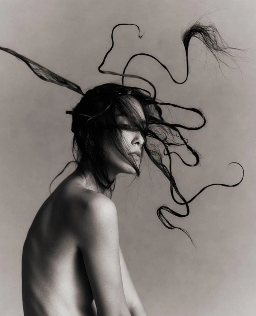 Artistic black-and-white portrait of a bare-shouldered woman with stylized hair, emphasizing creative beauty and photographic technique.