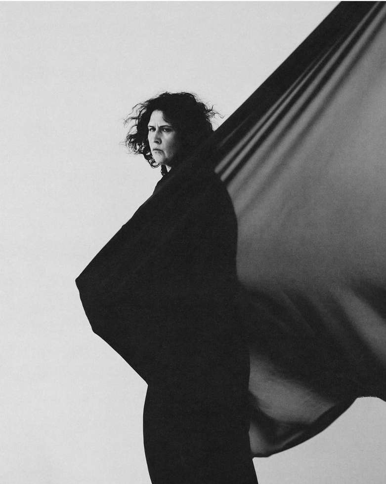 Monochromatic portrait of an adult woman draped in sheer black fabric against a white background in an indoor setting.