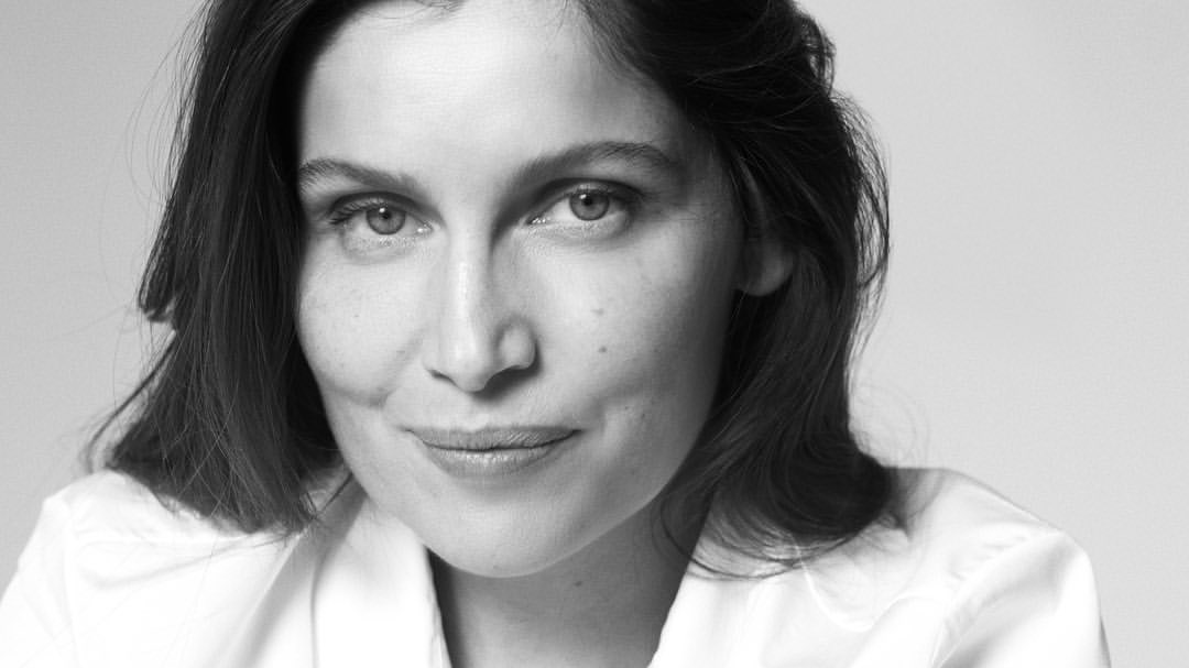Black and white portrait of a woman in a white collared shirt against a seamless light background by photographer Tess Ayano.