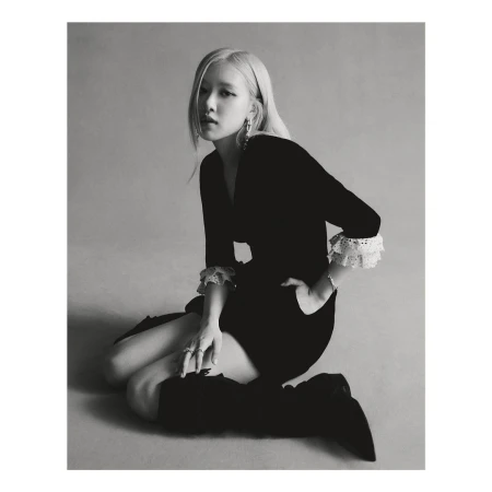 Black and white portrait of a blonde woman kneeling in a black dress with lace cuffs and high black boots, posing and looking at the camera.