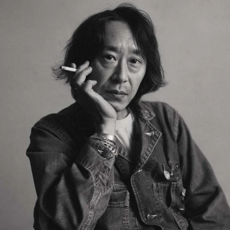 Black and white portrait of an Asian man holding a cigarette. He's wearing a denim jacket and silver bracelets against a neutral background.
