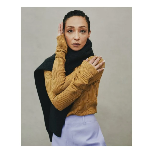 Portrait of adult woman in a golden sweater and black scarf posing with hands near her face in a photo studio setting. 