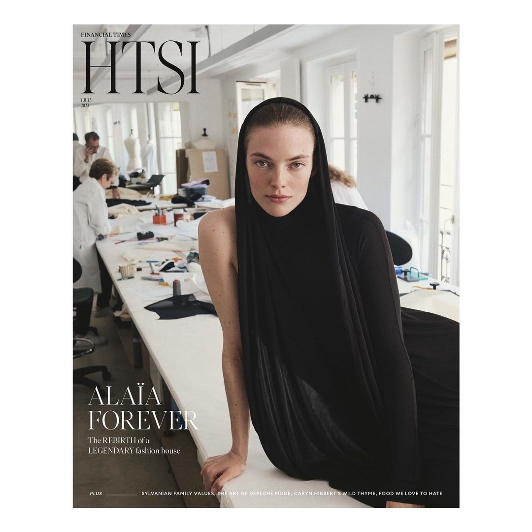 Magazine cover featuring a woman in a black headscarf with neutral expression, set against a workspace with sewing equipment.