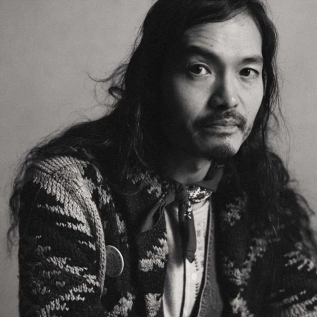 Portrait of a man with long dark hair wearing a patterned cardigan and a neckerchief by photographer Tess Ayano