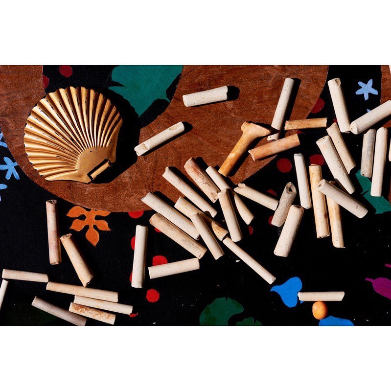 Overhead shot of a seashell with cylindrical objects scattered on a patterned surface featuring dots and organic shapes.