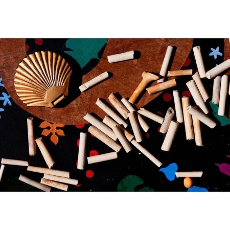 Overhead shot of a seashell with cylindrical objects scattered on a patterned surface featuring dots and organic shapes.